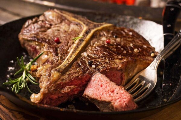 t bone steak that is on a plate and has peppercorns on it