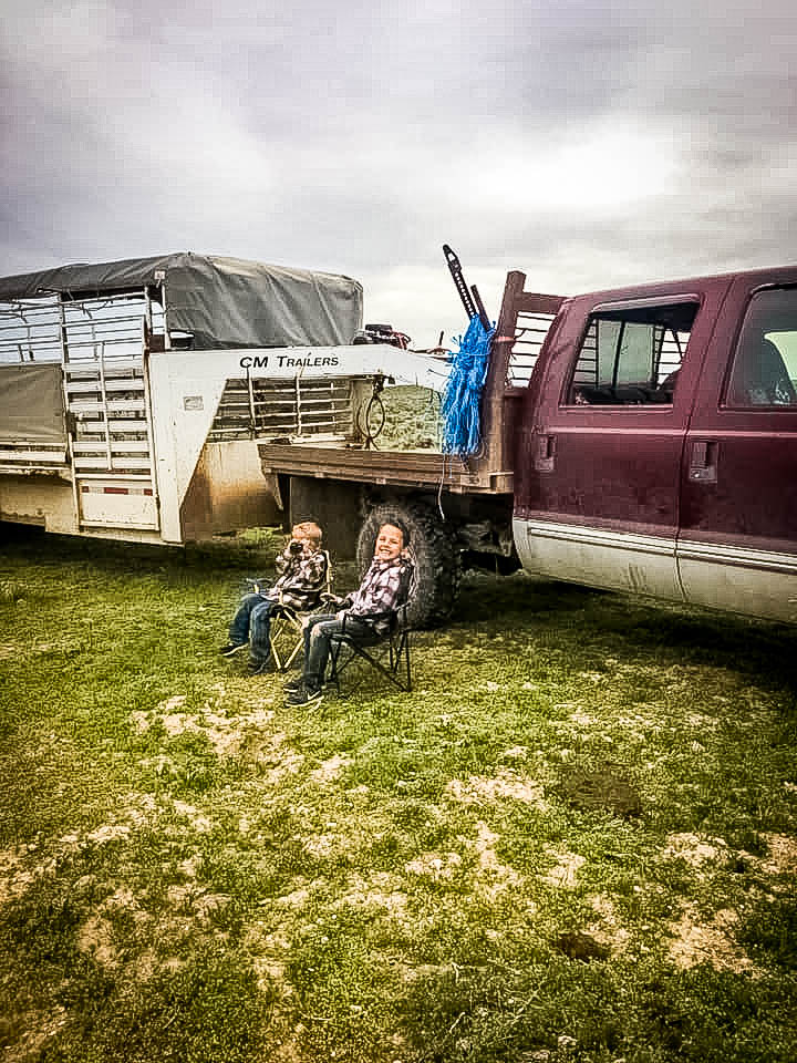 2 kids sitting in chairs on the hipwell ranch property with a truck and trailer in the background